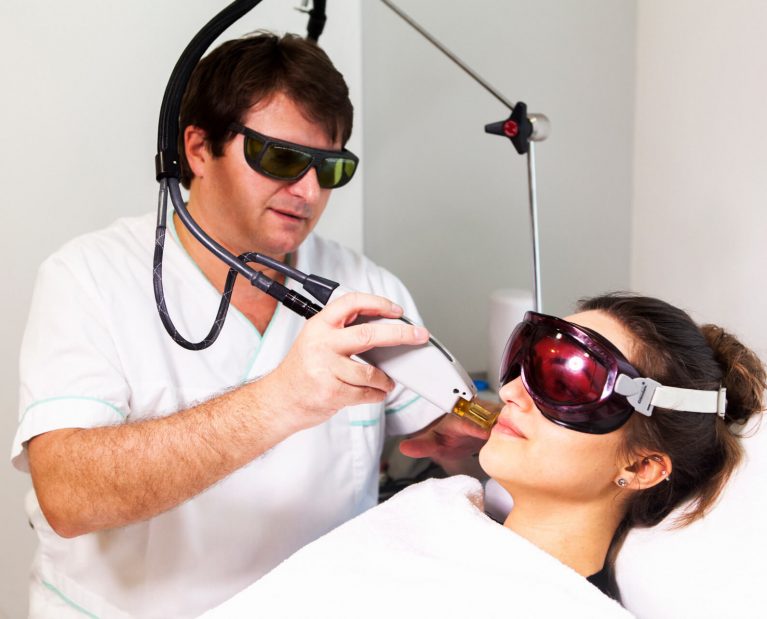 Žena podstupujúca laserovú depiláciu na tvári. Zákrok vykonáva pán doktor.